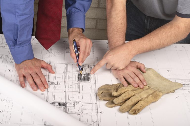Hands pointing at efficient architectural plans with a pair of work gloves nearby.
