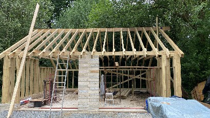 A partially constructed wooden building with a scaffold and trees in the background.