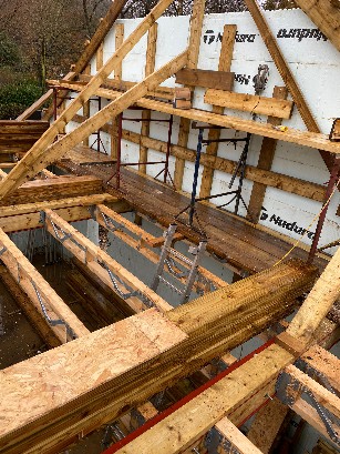 Construction site showing wooden framework and scaffolding for a house.