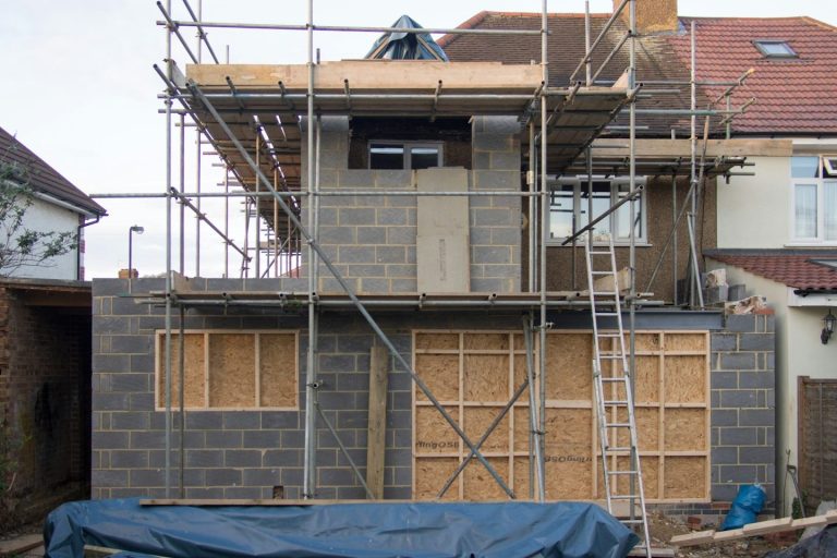 A house under construction with scaffolding and boarded windows.