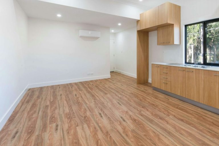 Spacious room with wooden flooring, a kitchenette, and natural light from large windows.
