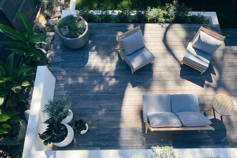 A wooden deck with two chairs and potted plants under natural light.