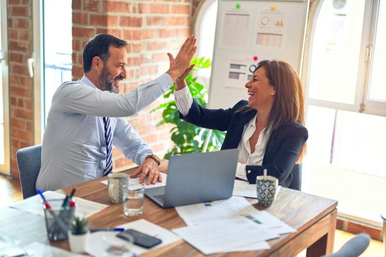 Colleagues sharing a quality high-five in a modern office setting, surrounded by papers and plants.