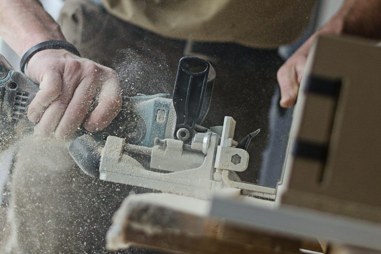 Person using a power tool to cut wood, with sawdust flying around.